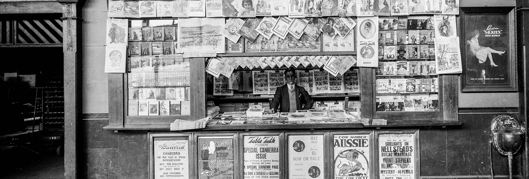 Black and white image of man working at newspaper stand, Spencer St train station