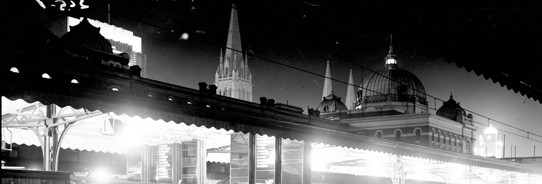 photo of melbourne at night from the view point of a train station platform, the dome of flinders street station can be seen in the distance