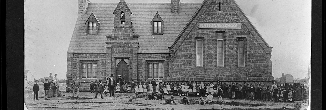 Black and white photograph of a nineteenth century school building with children outside