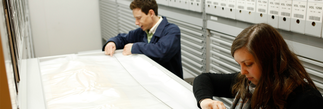 two people opening a plan drawer and looking over a map