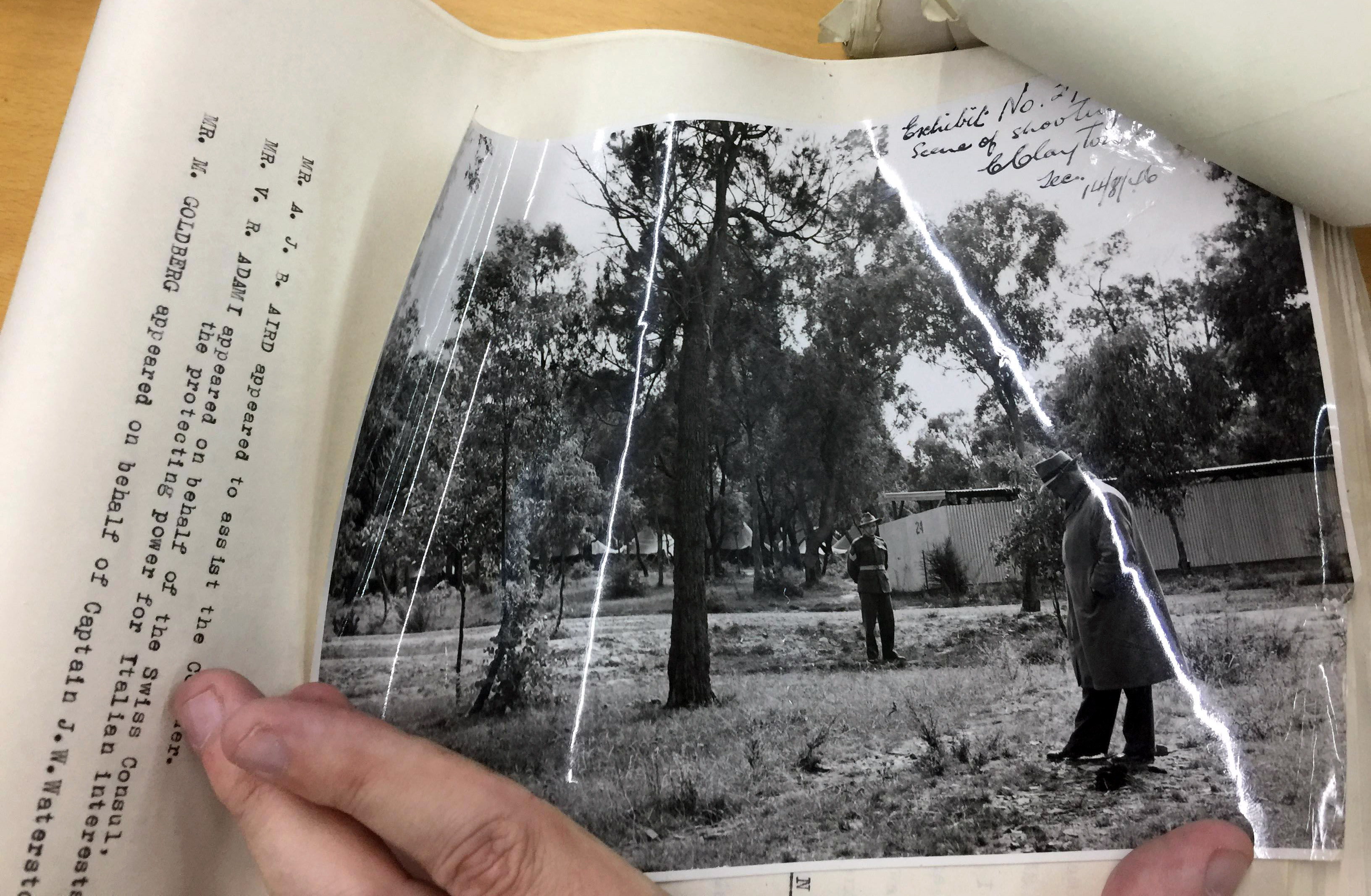 black and white photograph of police men looking at a dusty ground surrounded by trees