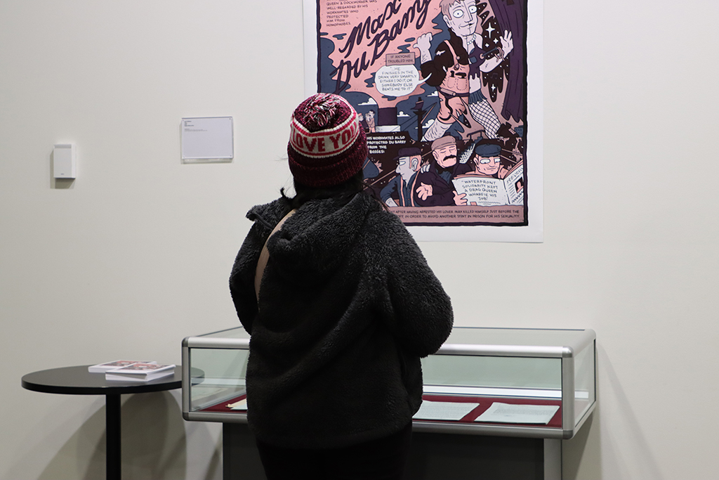 Rewind Forward exhibition. A personal is viewing a printed comic illustration hanging on the wall, above a cabinet of archival records.