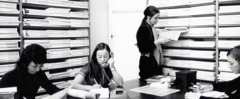 PMA employees PROV VPRS 8357 P1 Unit8 Item5/58 black and white photo of women working at a large desk with lots of paper work stacked behind them