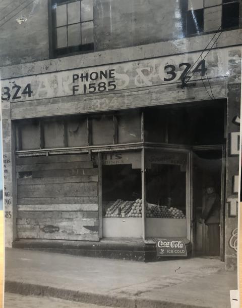 black and white photo of a shopfront that has been damaged and has wood across the front where the glass window should be