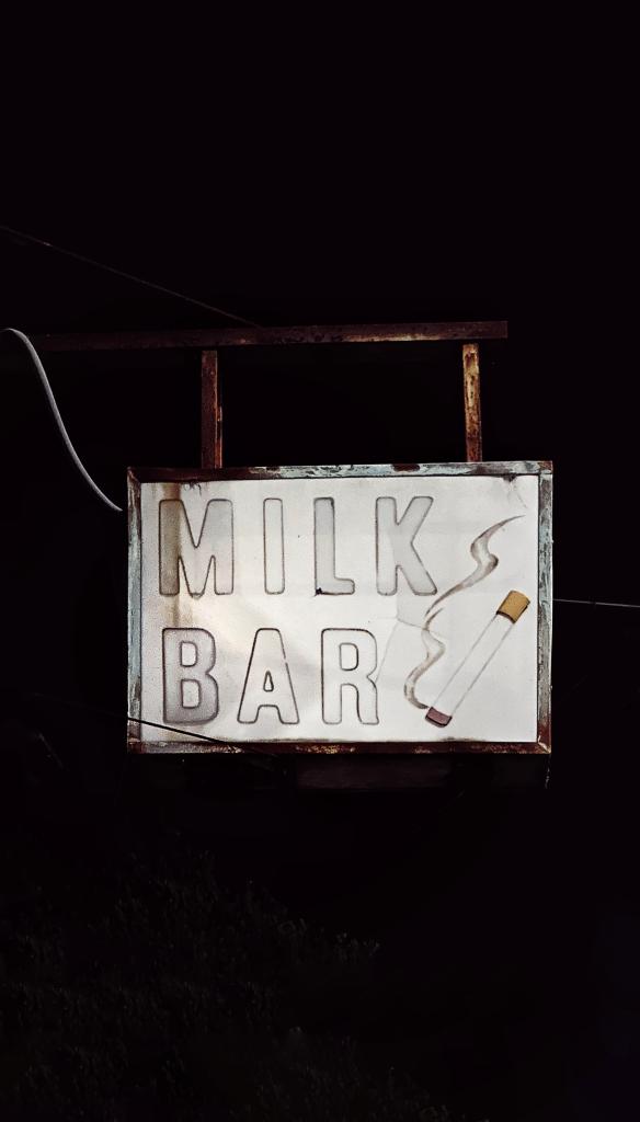 Photograph of an old sign, sign reads Milk Bar with a cigarette next to it