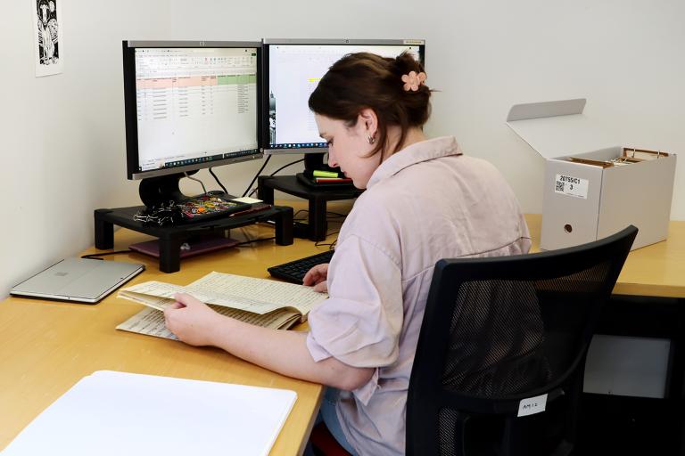 A woman looks through an archival record while sitting at a computer station
