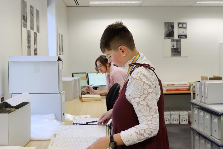 Two women working in an office space with archival records and boxes